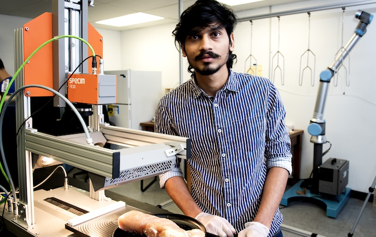 A man in a blue shirt operates a machine, focused on his task in a work environment.