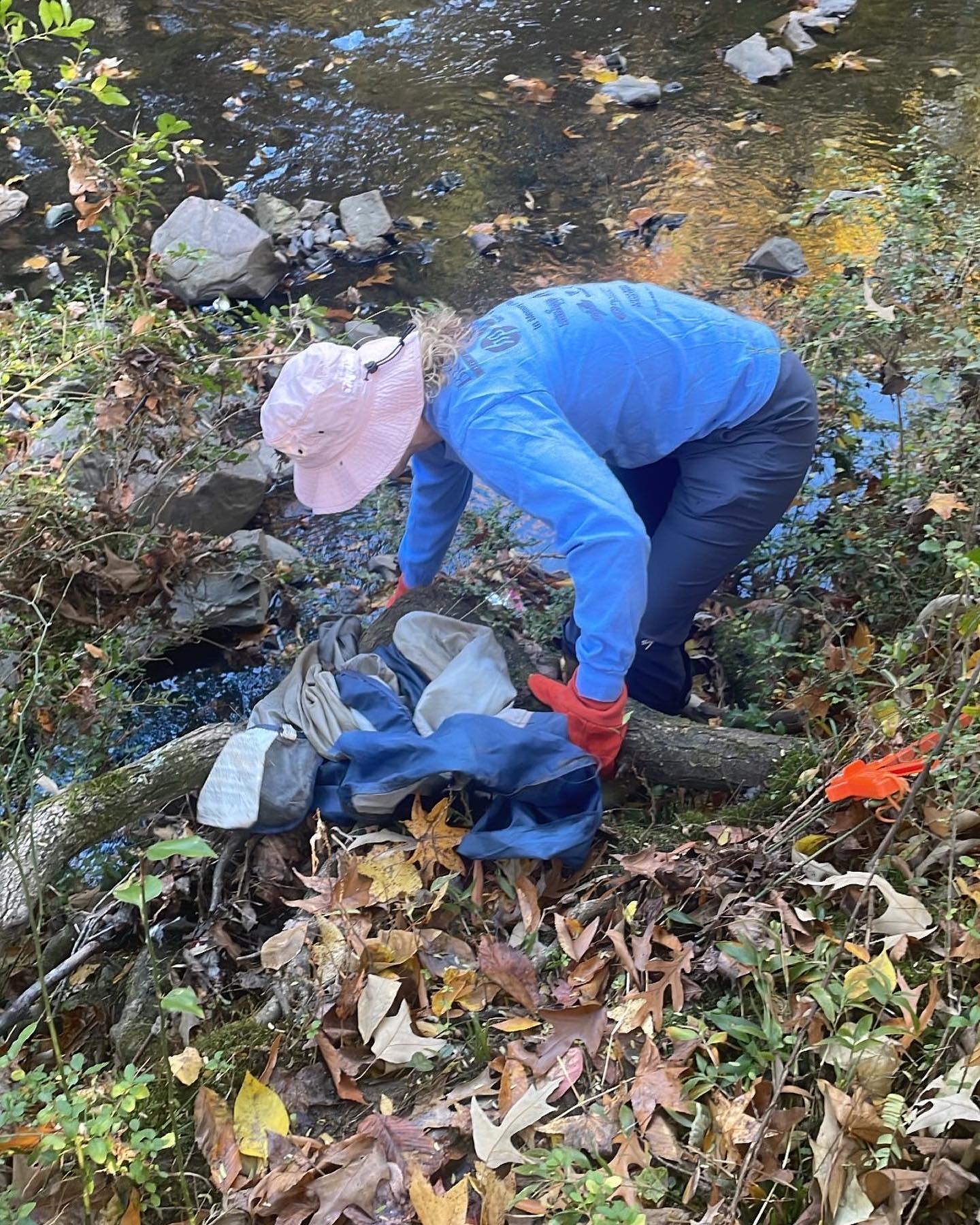 person in pink hat in creek bed picking up trash