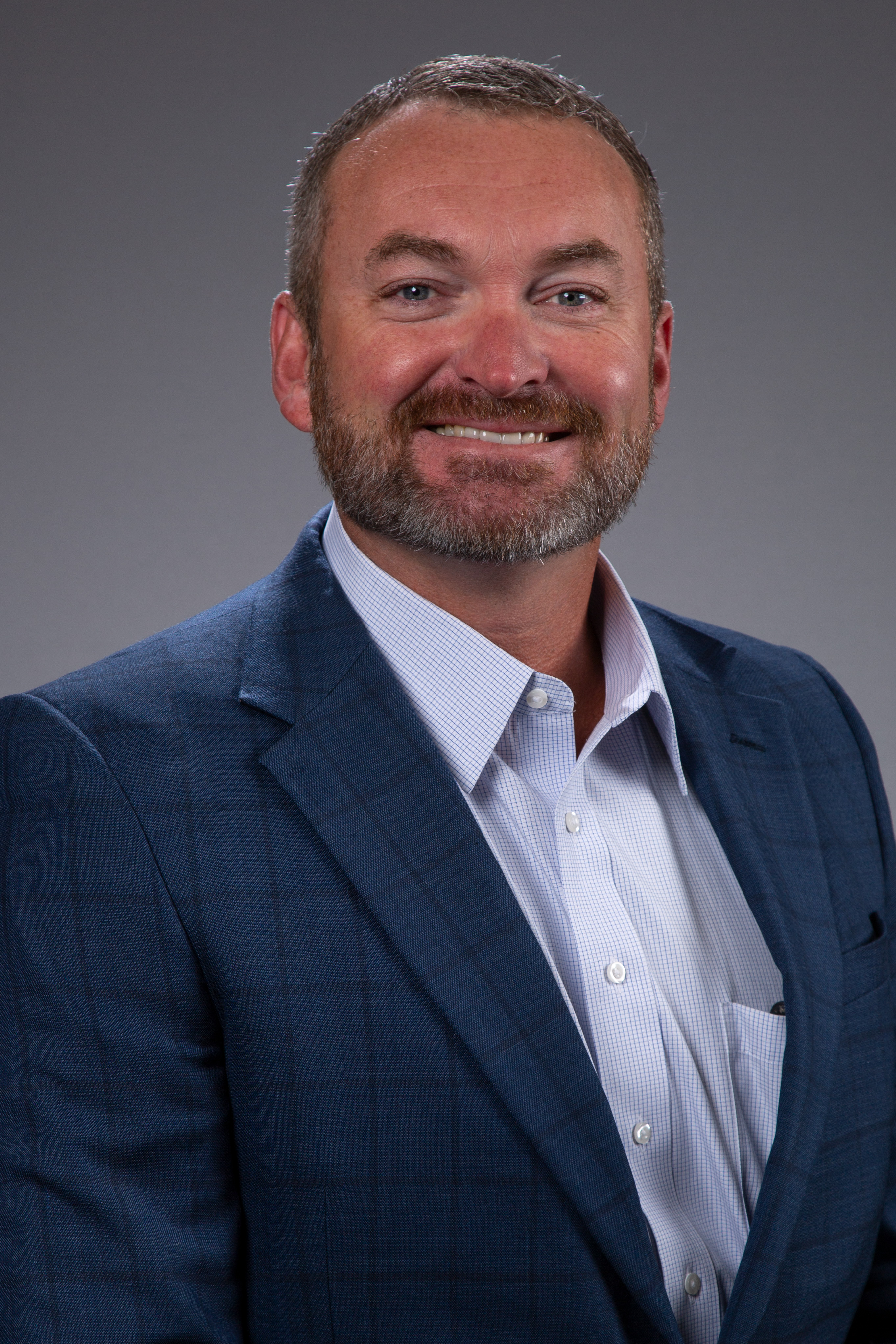 Smiling man with dark suit jacket, light shirt.