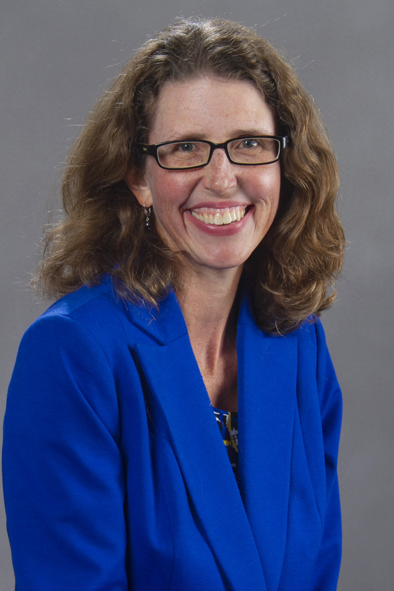 Woman with long hair, glasses wearing a royal blue top. 