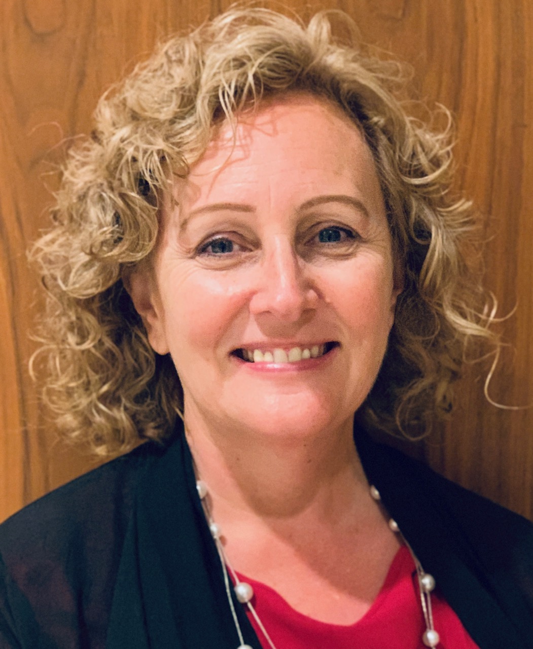 Portrait of Debbie Nistler, with blonde curly hair, dark jacket, red blouse