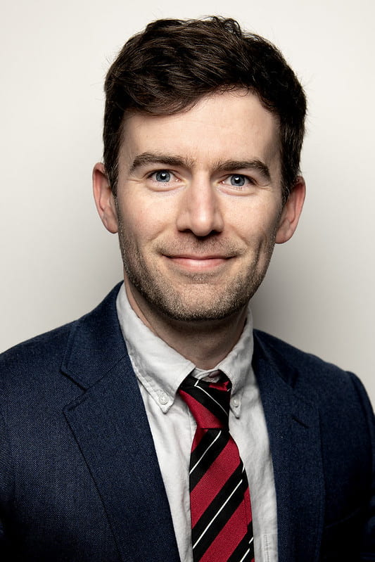 Portrait of Rich Adams, with dark coat, red tie, dark short hair