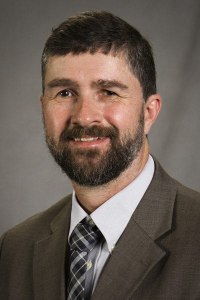 Portrait of bearded man with dark suit and tie.